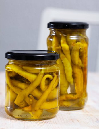 Glass jar of homemade marinated green chili peppers on wooden background