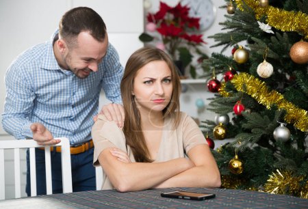 Lächelnder Mann beruhigt beleidigte Freundin nach Streit zu Hause an Heiligabend..