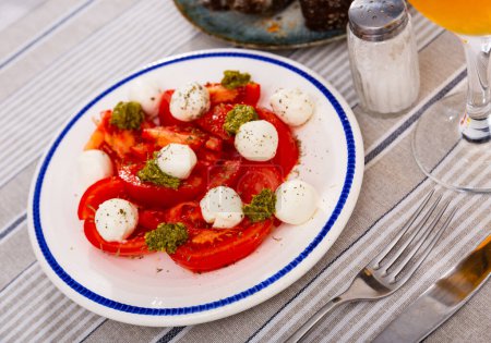 Service plate containing appetizing Caprese salad made of tomato and mozzarella with balsamic sauce