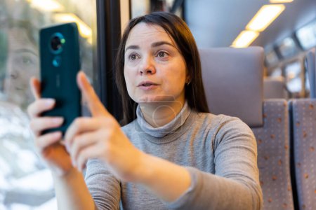 Frau fotografiert Blick aus Zugfenster mit ihrem Smartphone.