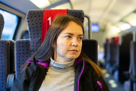 Portrait rapproché d'une femme brune contemplative décontractée voyageant en train express, assise sur un siège confortable et doux