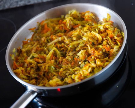 Closeup of braised white cabbage, stewed with carrots and onions in a pan on a kitchen stove