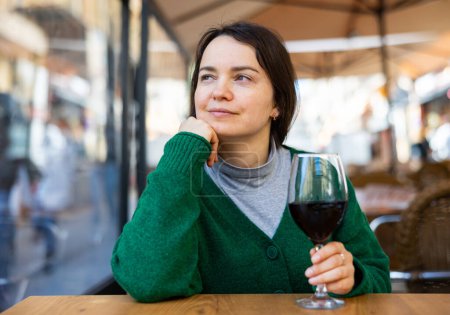 Portrait of cheerful woman enjoying red wine on cafe terrace