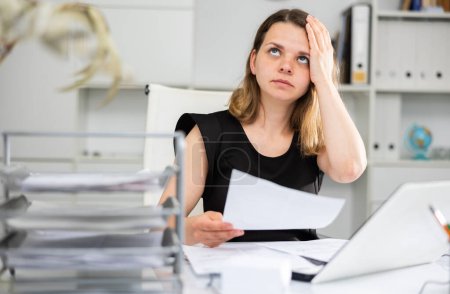 Upset woman working with laptop and papers at the office