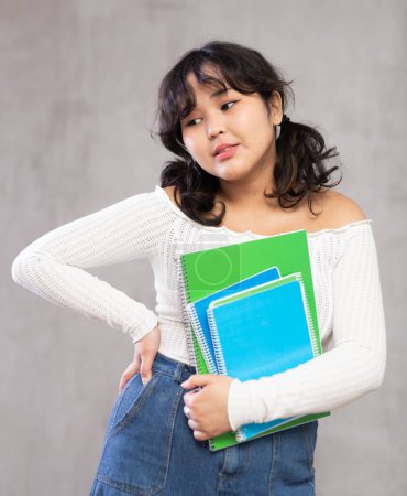 Portrait of pensive asian girl in casual clothes posing with notebooks in studio