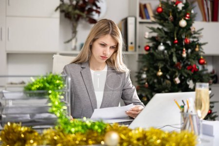Female office worker sitting at desk and doing paperwork during Christmastime.