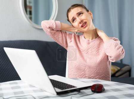 Young woman experiencing neck pain after working on laptop at home