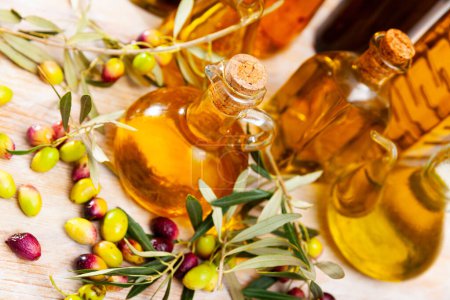 Dekanter und Flaschen mit goldenem Olivenöl garniert mit reifen Oliven auf Holzoberfläche