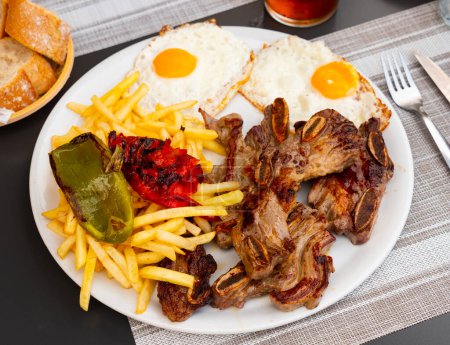 Delicious grilled pork ribs served on plate with side dish of fried eggs, french fries and baked peppers. Popular Spanish combination meal with churrasco