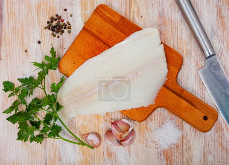 Filet de flétan cru, ail, persil sur table en bois. Ingrédients pour la cuisine