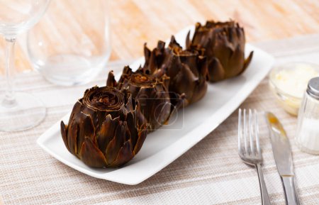 Appetizing dish of Mediterranean cuisine baked artichokes, served with sauce and salt