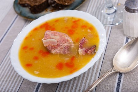 delicious pea soup with smoked meats and orange carrots cools down in white ceramic plate