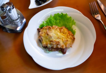 Appetitlich französisches Fleisch mit Pilzen in Mornay-Käsesauce, serviert auf frischem grünen Salatblatt. Festliche russische Küche