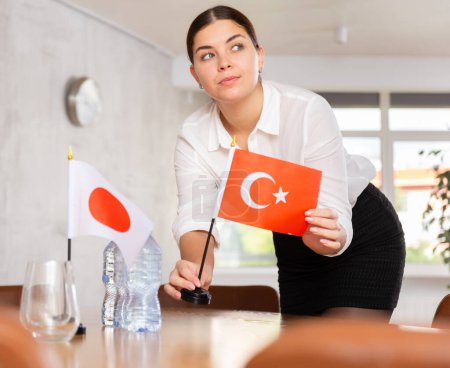 Mujer joven colocando banderas sobre la mesa para las negociaciones internacionales entre Japón y Turquía