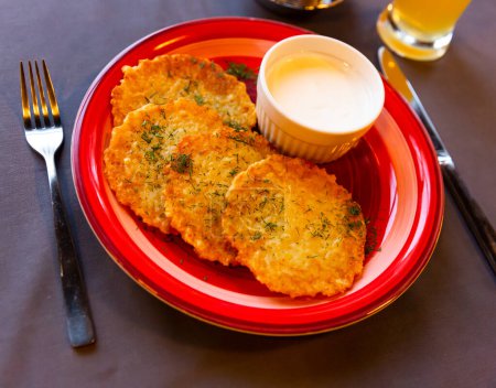 Draniki, potato fritters with with yogurt sauce served in red plate. Belarusian cuisine