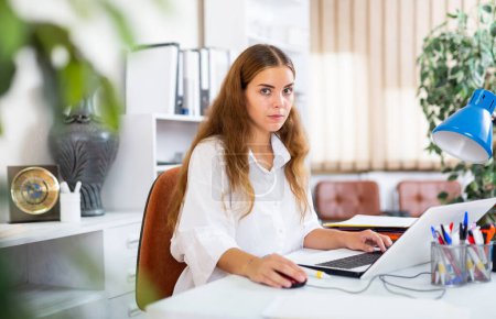Female bookkeeper sitting at desk in office and working on computer.