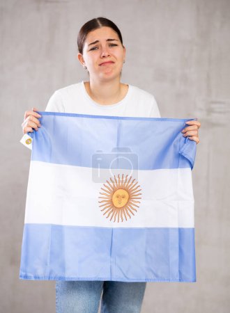 Jeune femme irrité avec le drapeau argentin derrière les épaules. Isolé sur fond gris