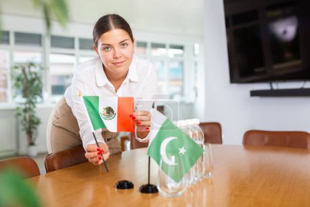 Young woman in business clothes puts flags of Mexico and Pakistan on negotiating table in office