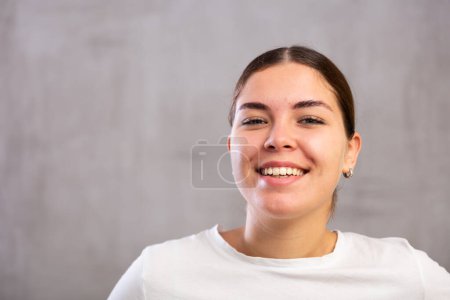 Nahaufnahme Foto einer fröhlichen jungen Frau, die glücklich vor grauem, schattenlosen Hintergrund posiert
