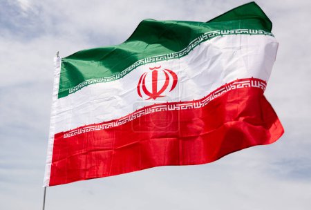 Grand drapeau de l'Iran attaché sur bâton sur fond de ciel bleu sous la lumière du jour
