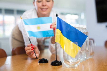 Preparación de las negociaciones internacionales. Coordinador de la oficina poniendo banderas nacionales de Ucrania y Argentina en la mesa, tiro recortado. Concepto de relación diplomática entre países