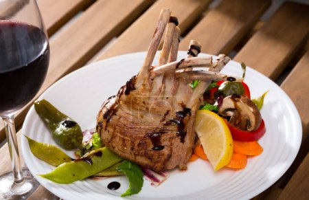 Appetizing baked rack of lamb with roasted and fresh vegetables, greens, lemon and balsamic served with red wine