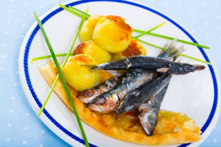 Roasted pilchards served on plate with fried mashed potato balls and focaccia..