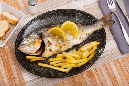 Delicious baked sea fish called Dorada, served with French fries and lemon slices