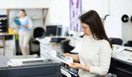 Druckereileiter steht am Drucker und betrachtet die Farbprüfseite für Drucker.