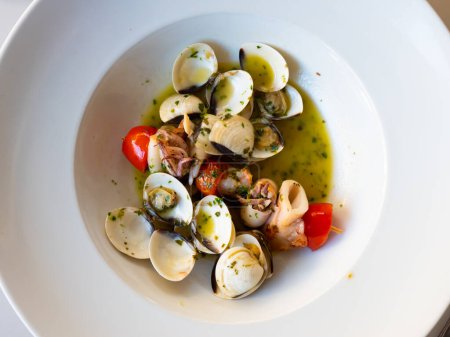 Mediterranean cuisine, squid skewer with garlic and clams in a white ceramic plate