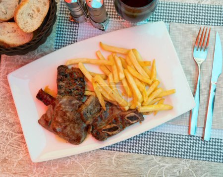 Serving of parillada de carne on white plate with some wine and and bread
