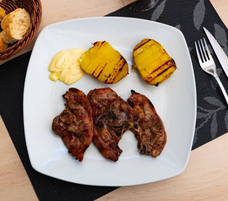 Grilled lamb thigh and some potatoes served in a plate with other table appointments