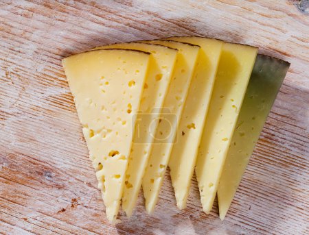 Slices of semi-hard cheese from milk of sheep on wooden background..