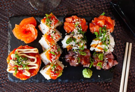 Traditionelle japanische Sushi-Platte. Gunkanmaki mit verschiedenen Füllungen, Uramaki und rohem Lachssashimi auf Schiefertafel
