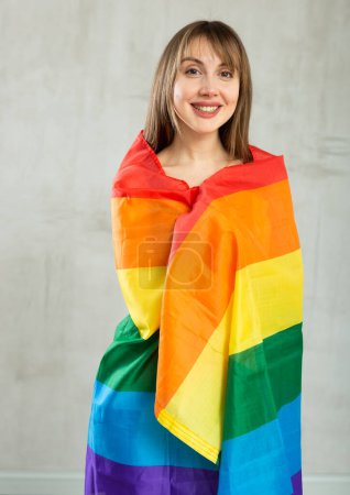 Happy young woman with large transgender flag posing gladly against light unicoloured background