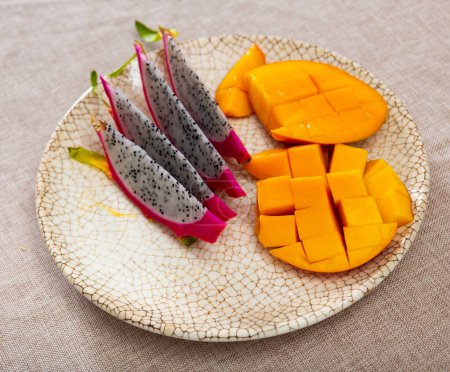 Gesunde bunte, lebendige Snacks aus tropischen Früchten. Scheiben gelb-orange Mango und rosa Pitaya mit kleinen schwarzen Samen auf dem Teller