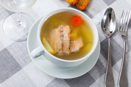 Appetizing rich salmon backbone soup with potatoes and carrots served in white tureen with crispy toasts ..