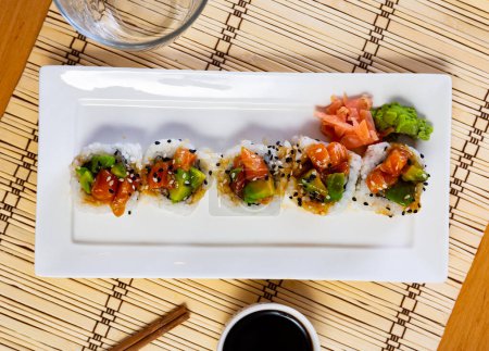 Traditionelle japanische Sushi-Rollen, gefüllt mit Krabbenfleisch und Gurken, garniert mit Lachs und Avocado, gewürzt mit würziger Unagi-Sauce, bestreut mit Weißem 