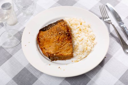 Gebratenes Thunfischsteak mit Unagi-Sauce bestreut mit Sesam und gekochtem weißen Reis. Abendessen inspiriert von japanischen Aromen..