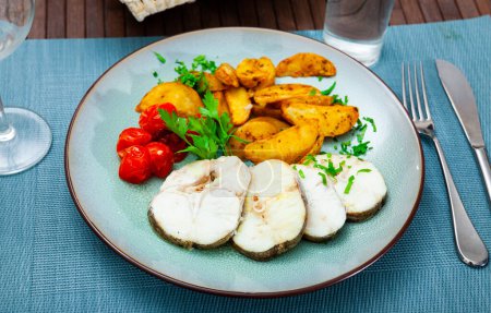 Baked hake steaks with vegetable side dish of spicy potato wedges, marinated tomatoes and fresh greens