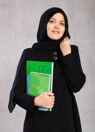 Retrato de una joven estudiante sonriente en hijab posando con cuadernos en el estudio