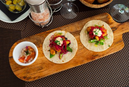 Mexican tacos made of shrimps, Chipotle mayonnaise and vegetables, served on table and ready-to-eat.