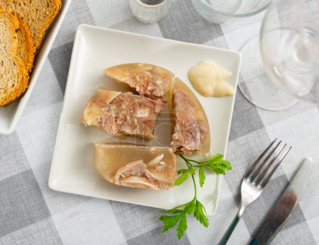 Traditional russian meat aspic dish kholodets on plate with mustard and parsley.