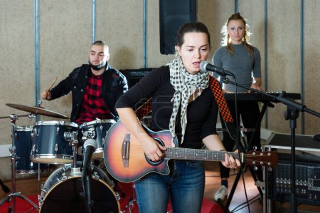 Probe der Musikkapelle. Aktive Gitarristin und Sängerin üben mit Bandmitgliedern im Tonstudio