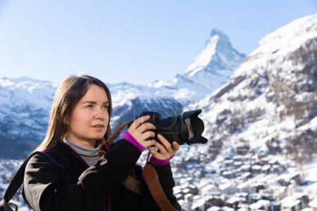 Mujer viajera con pasión por la fotografía disfrutando del senderismo en los Alpes suizos en invierno, tomando fotos de la naturaleza con cámara profesional
