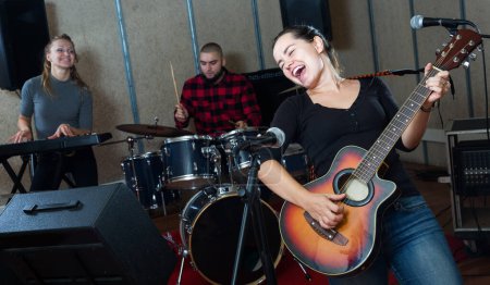 Banda de música garage con apasionada mujer emocional vocalista y guitarrista ensayando en estudio de sonido