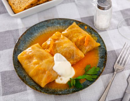 Cabbage rolls with sour cream and parsley served on plate. Russian cuisine dish on table.