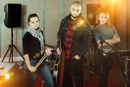 Expressive active adult group of rock musicians posing with instruments in recording studio