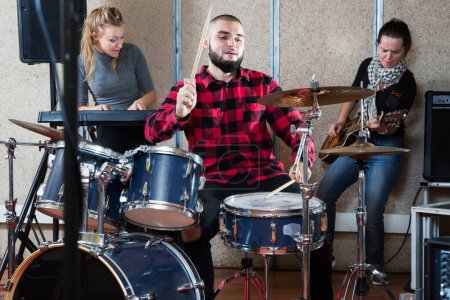 Music garage band with expressive male drummer practicing in sound studio