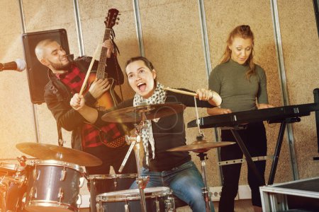 Emocional apasionada alegre alegre positiva sonriente baterista femenina con sus compañeros de banda practicando en la sala de ensayo